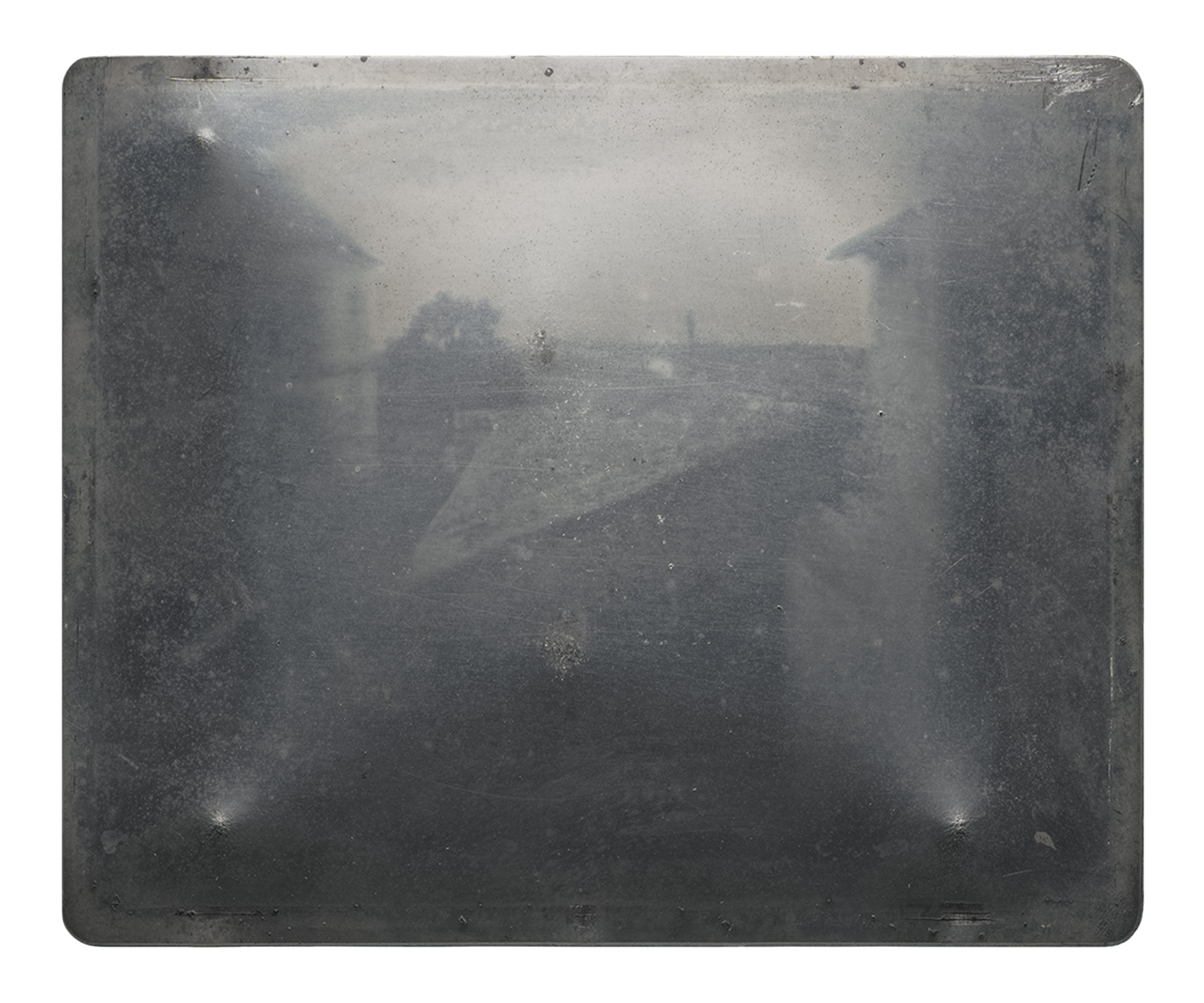View from the Window at Le Gras showing some buildings and a tree in the distance. This image has been flipped from the original metal plate along both the horizontal and vertical axes. The camera obscura would have originally recorded the upper right corner in the lower left corner. Public Domain.
